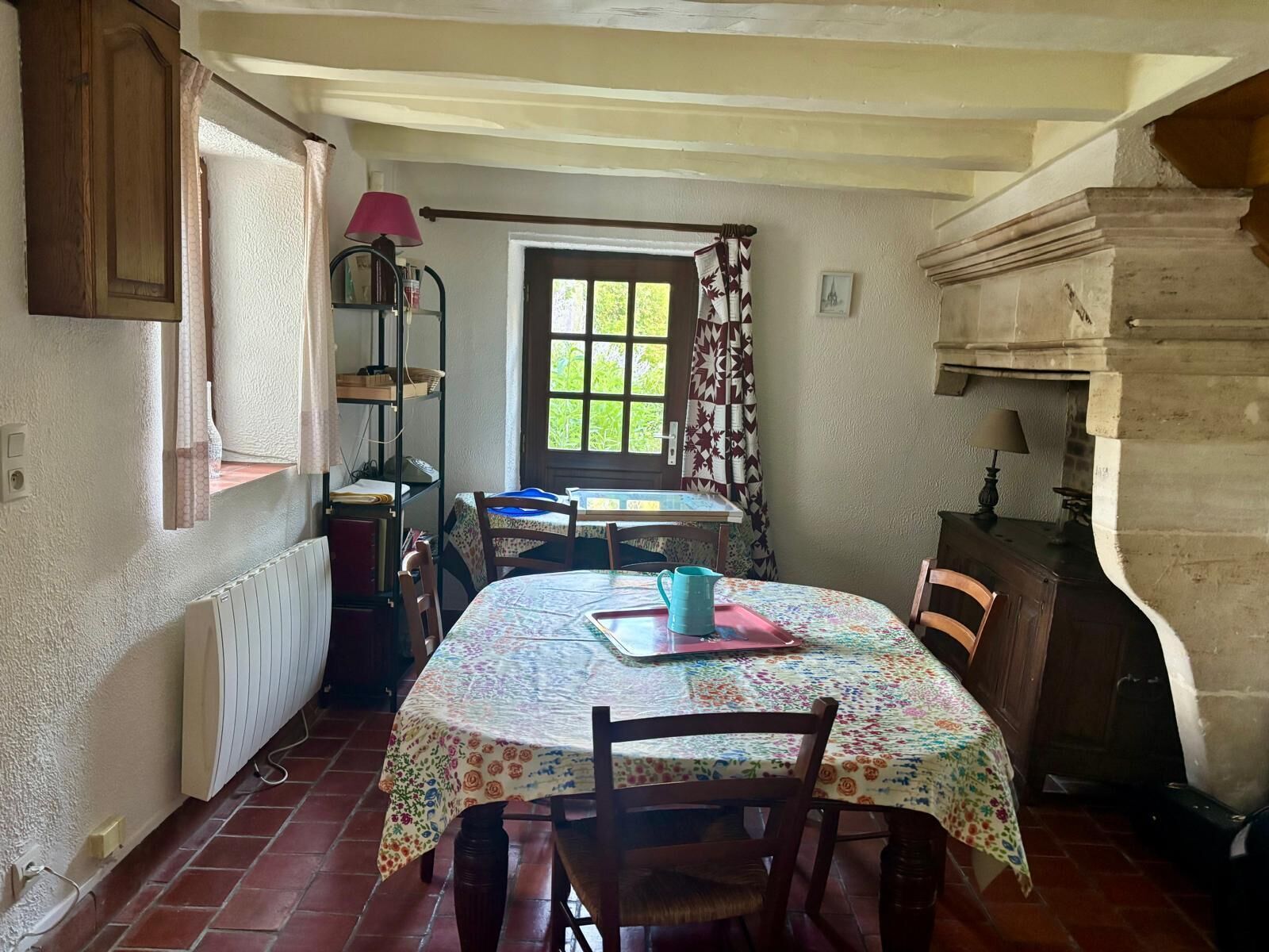 A dining area with a table set for two, a radiator, a window with curtains, and a fireplace.