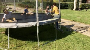 Un trampoline installé dans un espace extérieur enherbé, entouré d’un filet de protection.