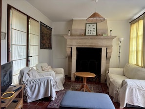 A living room with a fireplace, two sofas, a small table, and a television. - Charming vacation home with a pool in a park, recognized for its remarkable garden (Nettancourt)
