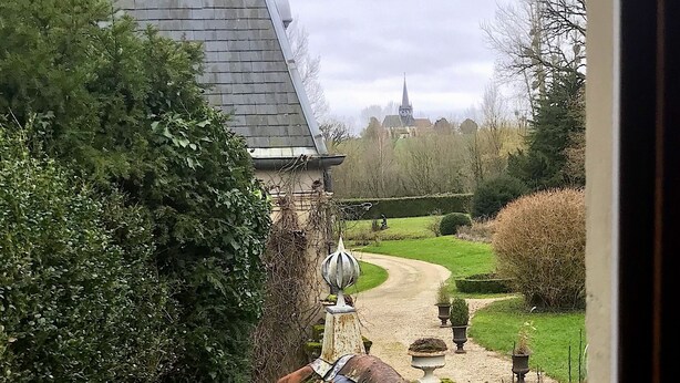 Une vue d’un jardin avec un sentier menant à un bâtiment dont le toit est recouvert de tuiles.