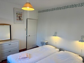 Una camera d'albergo con un letto, una cassettiera, uno specchio, una porta e lampade a parete.
