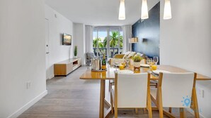 A modern dining area with a wooden table, white chairs, and hanging pendant lights. - Modern Resort | Gym and Pool | Near Beach (Hallandale Beach)