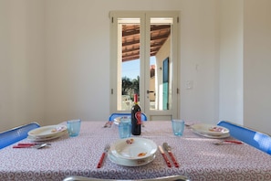 A dining table set with plates, cutlery, and a bottle of wine, with a view of the outside through a door. - 1755 Casina Farnarari - Appartamento 1 by Barbarhouse (Monteroni di Lecce)