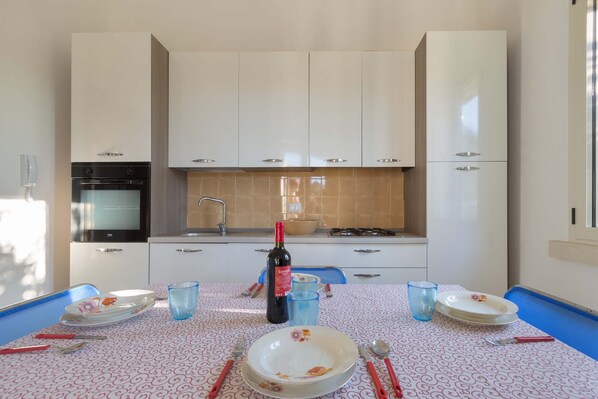 A modern kitchen with white cabinets, a built-in oven, and a dining table set with plates, glasses, and cutlery.