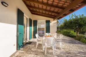 Eine Terrasse im Freien mit Steinboden, weißen Plastikstühlen und einem Tisch.