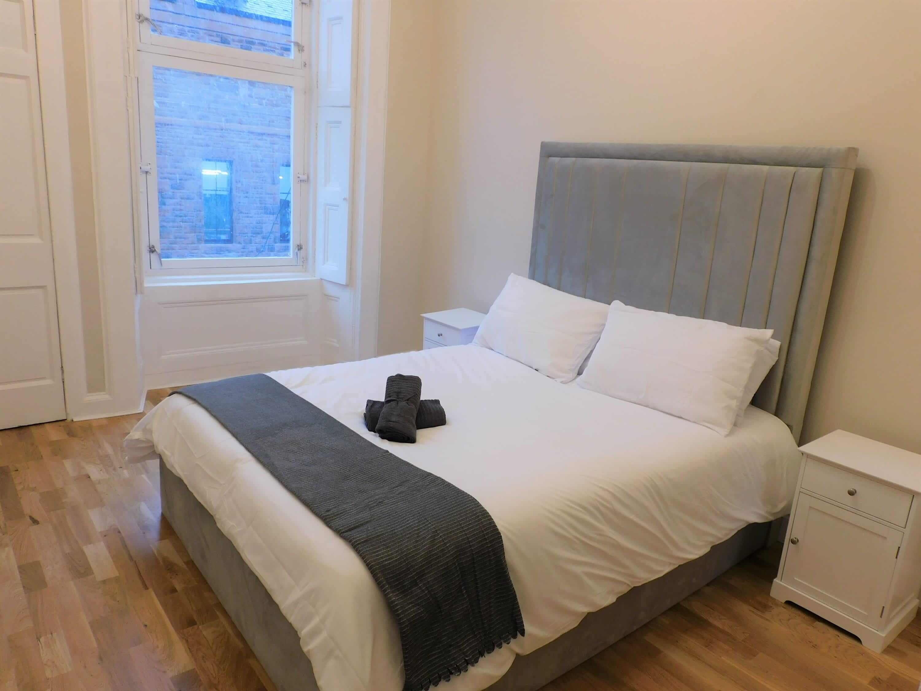 A bedroom with a bed, a nightstand, a window, and a door.