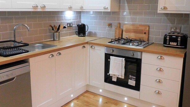 A modern kitchen with white cabinets, a gas stove, a toaster, and a dishwasher.