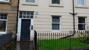 A multi-story residential building with a front door, windows, and a black metal fence.