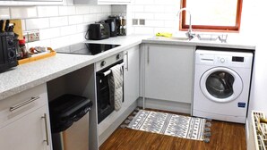 A compact kitchen with white cabinets, a built-in oven, a washing machine, and a window above the sink. - Charming  2 bed apt close to City and SEC/Hydro (Glasgow)