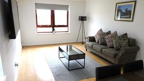 A living room with a sofa, a coffee table, a TV, a floor lamp, and a framed picture on the wall. - Charming  2 bed apt close to City and SEC/Hydro (Glasgow)