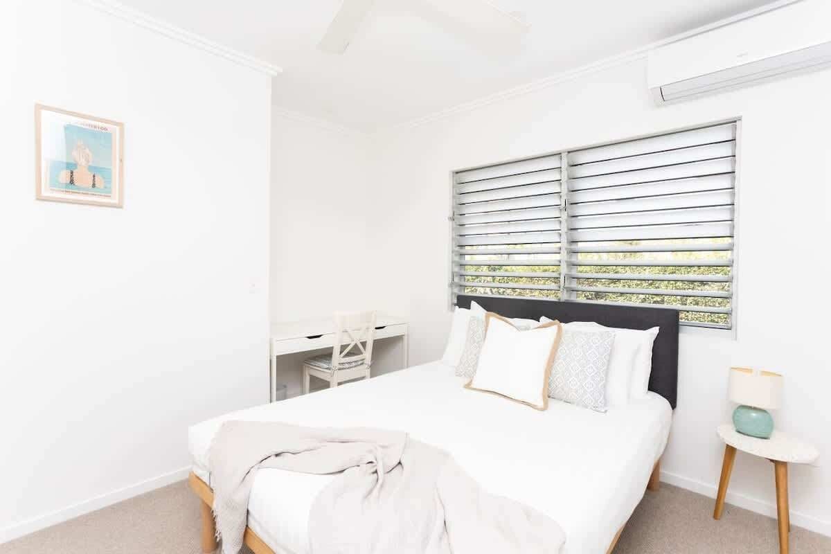 A bedroom with a bed, a desk, and a window with blinds.