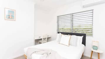 A bedroom with a bed, a desk, and a window with blinds.
