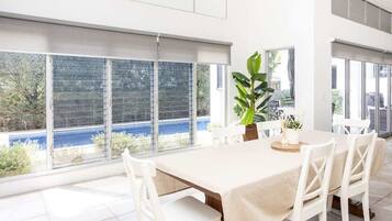 A dining area with a table set for four, large windows with blinds, and a view of a blue body of water.