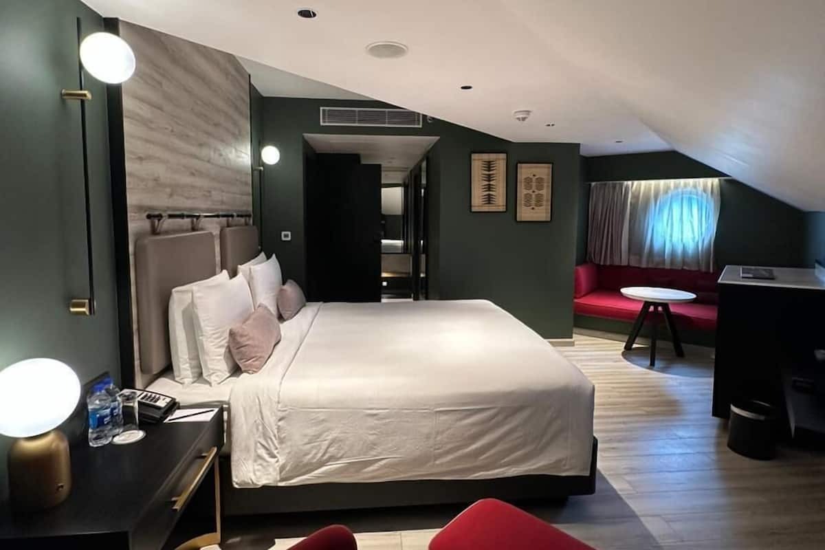 Ein modernes Hotelzimmer mit einem großen Bett, einem Schreibtisch, einem roten Sessel und einem kleinen Tisch.