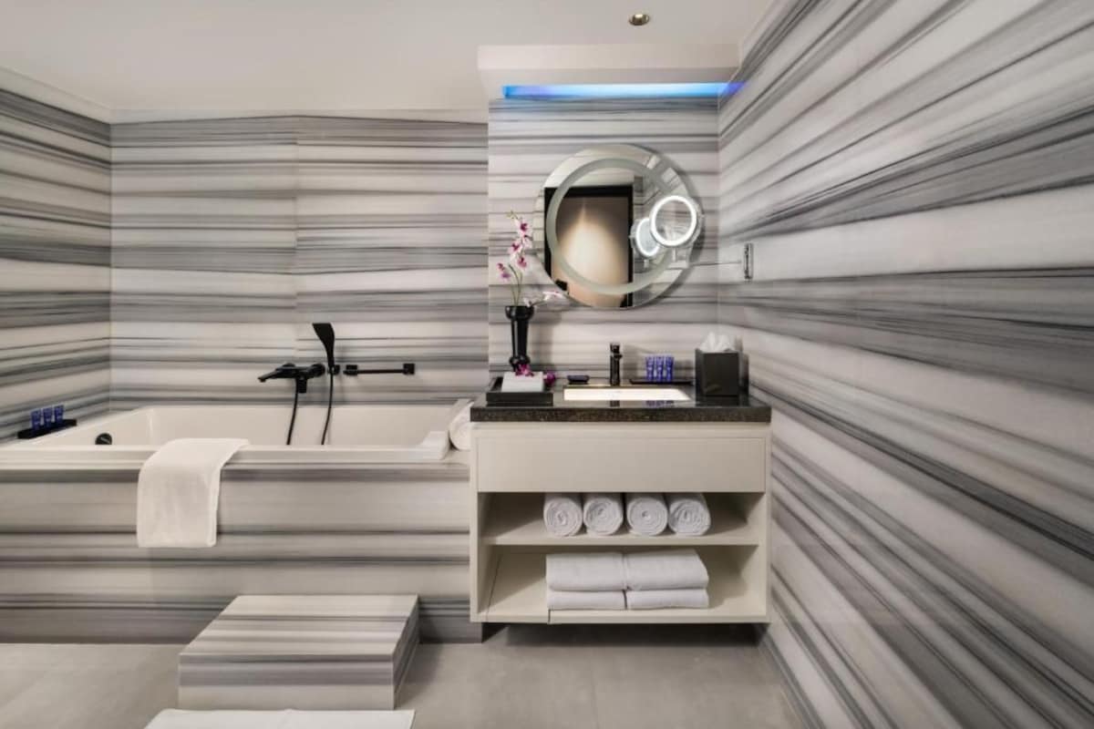 Une salle de bain moderne avec un mur en marbre, une baignoire, un meuble-lavabo avec un miroir et une étagère avec des serviettes.