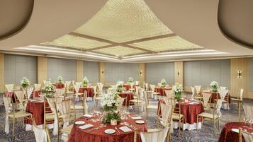 A banquet hall with round tables, gold chairs, and red tablecloths.