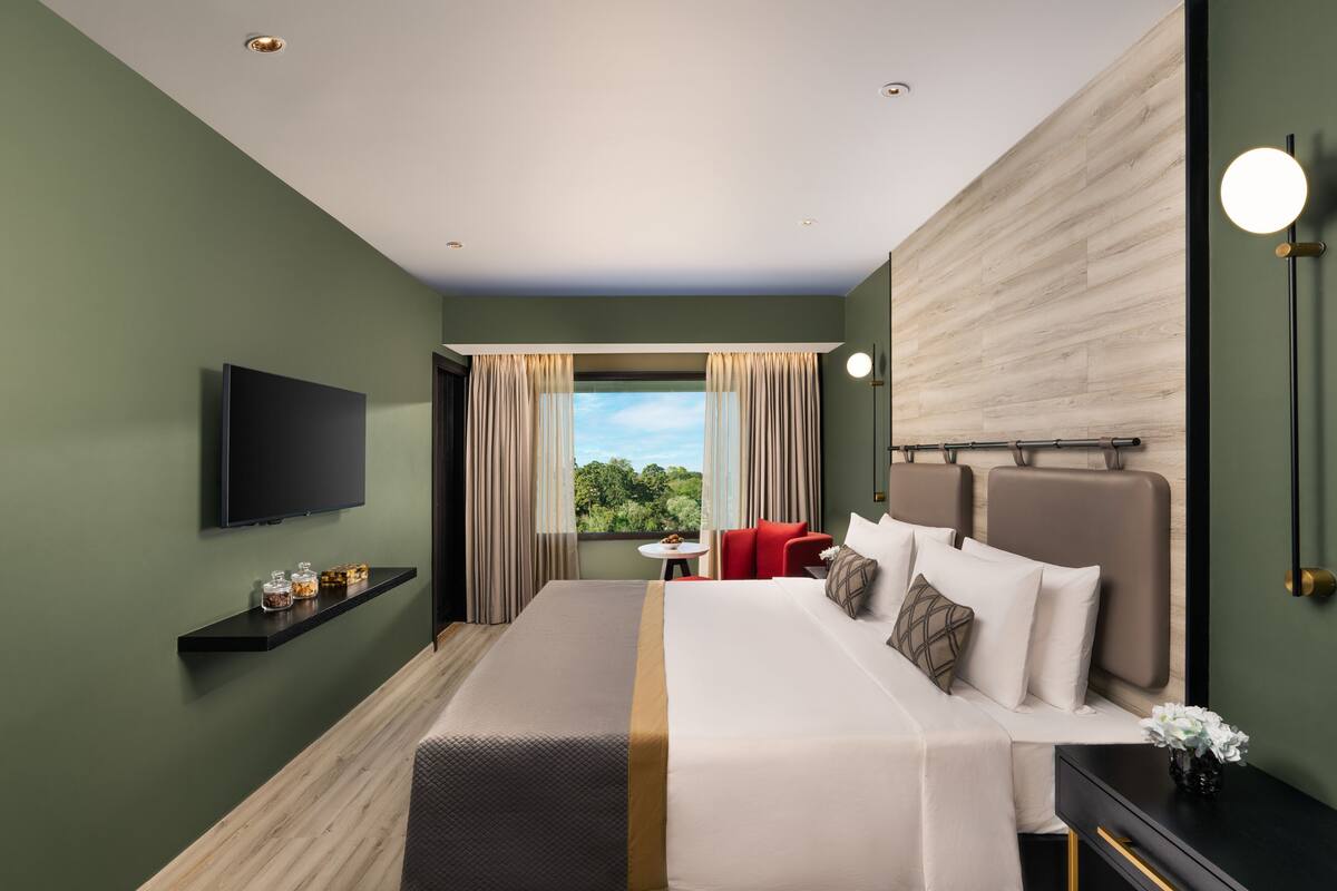 Ein Hotelzimmer mit einem großen Bett, einem Fernseher, einem kleinen Tisch und Blick ins Freie.