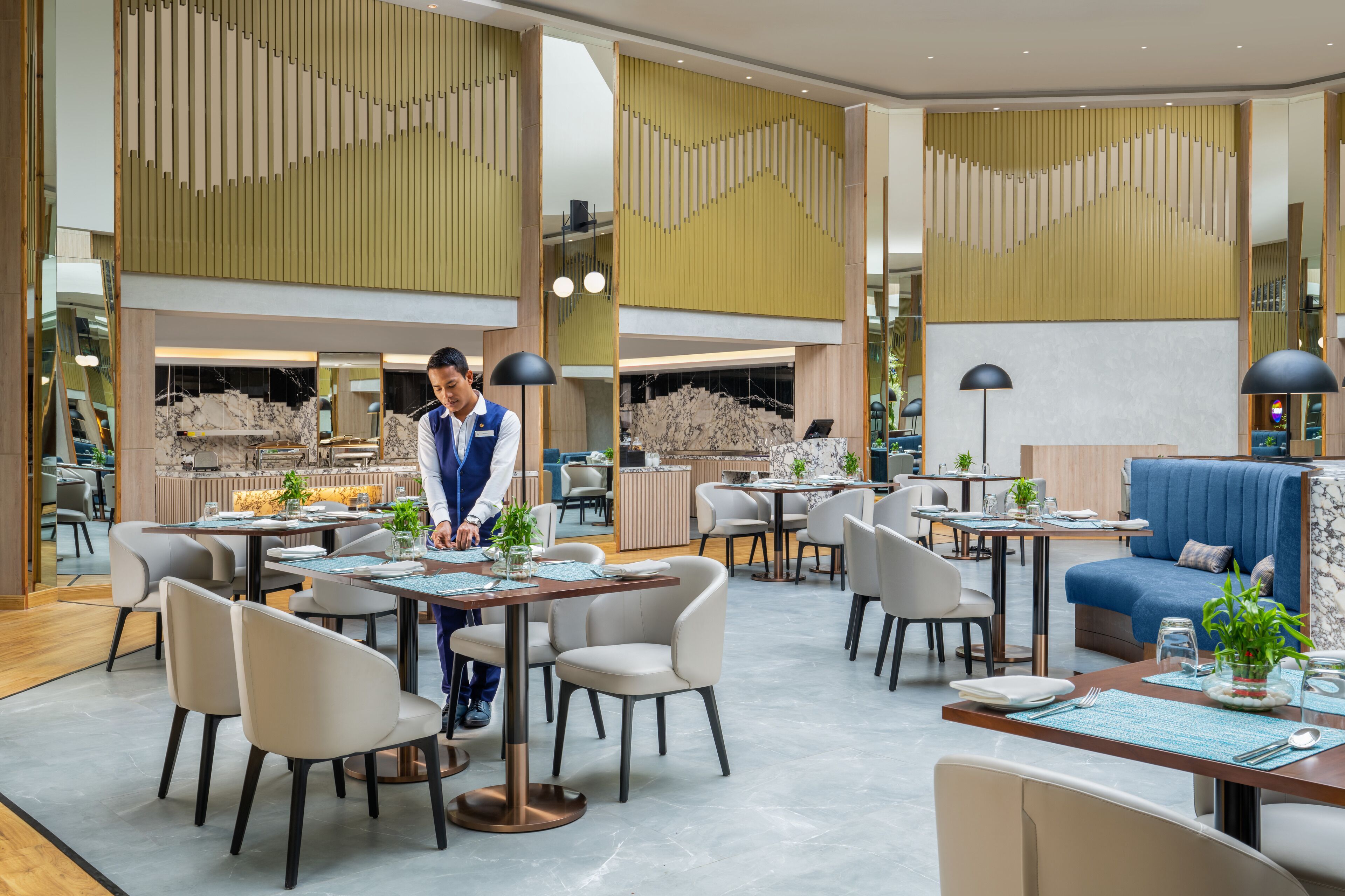Una zona d'esmorzar moderna amb diverses taules i cadires, una recepció i un espai d'estar amb un sofà blau.