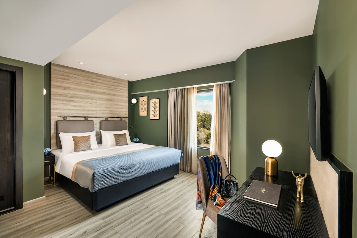 Ein modernes Hotelzimmer mit einem großen Bett, einem Schreibtisch mit Lampe und Blick ins Freie.