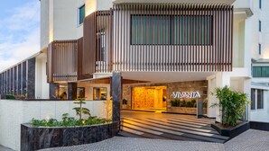 Een moderne hotelentree met een opvallend 'VINTA' bord, een overdekt buitenverblijf met beplanting, en een gevel van natuursteen.