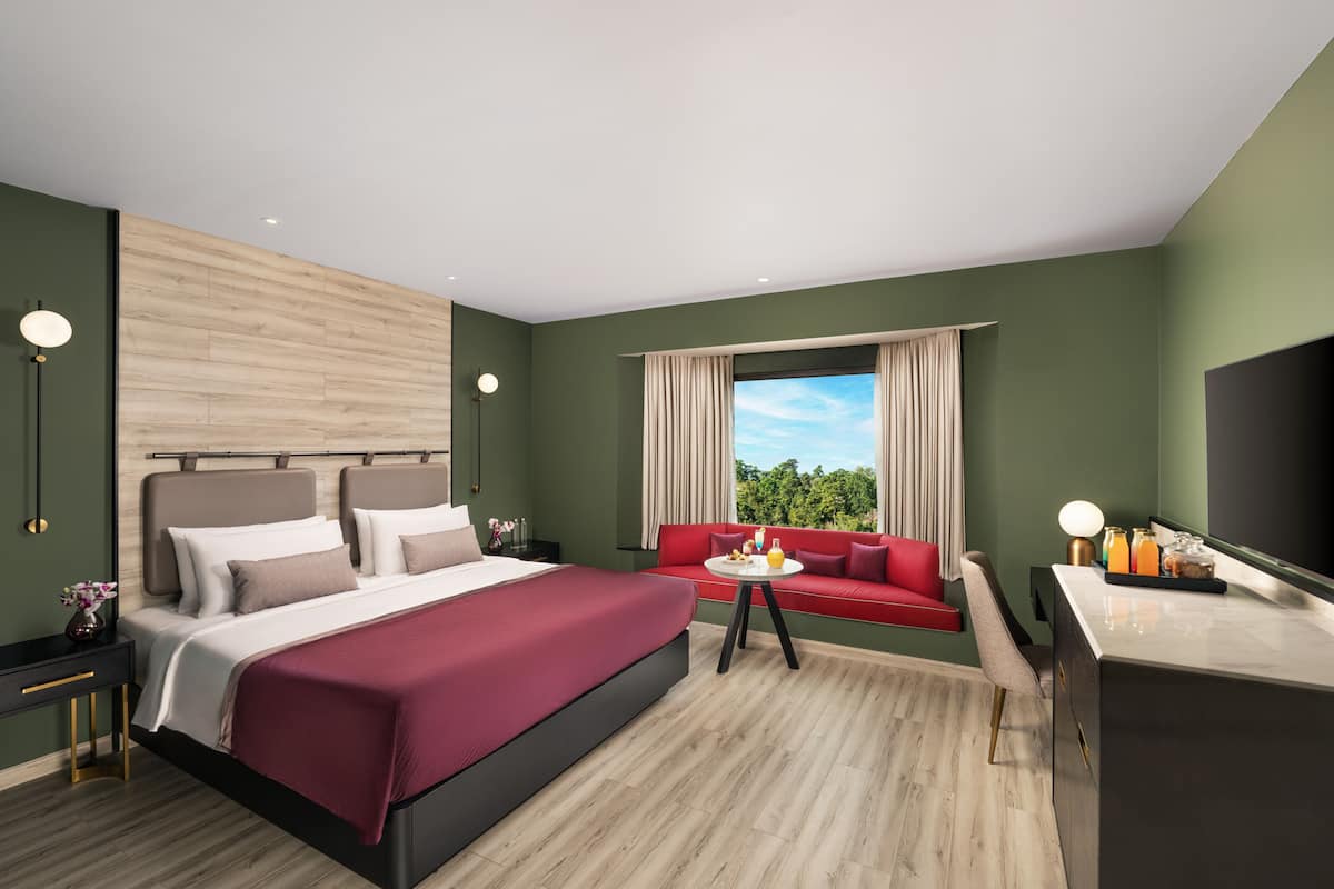 Ein modernes Hotelzimmer mit einem großen Bett, einer roten Couch, einem kleinen Tisch mit Getränken und einem Fernseher.