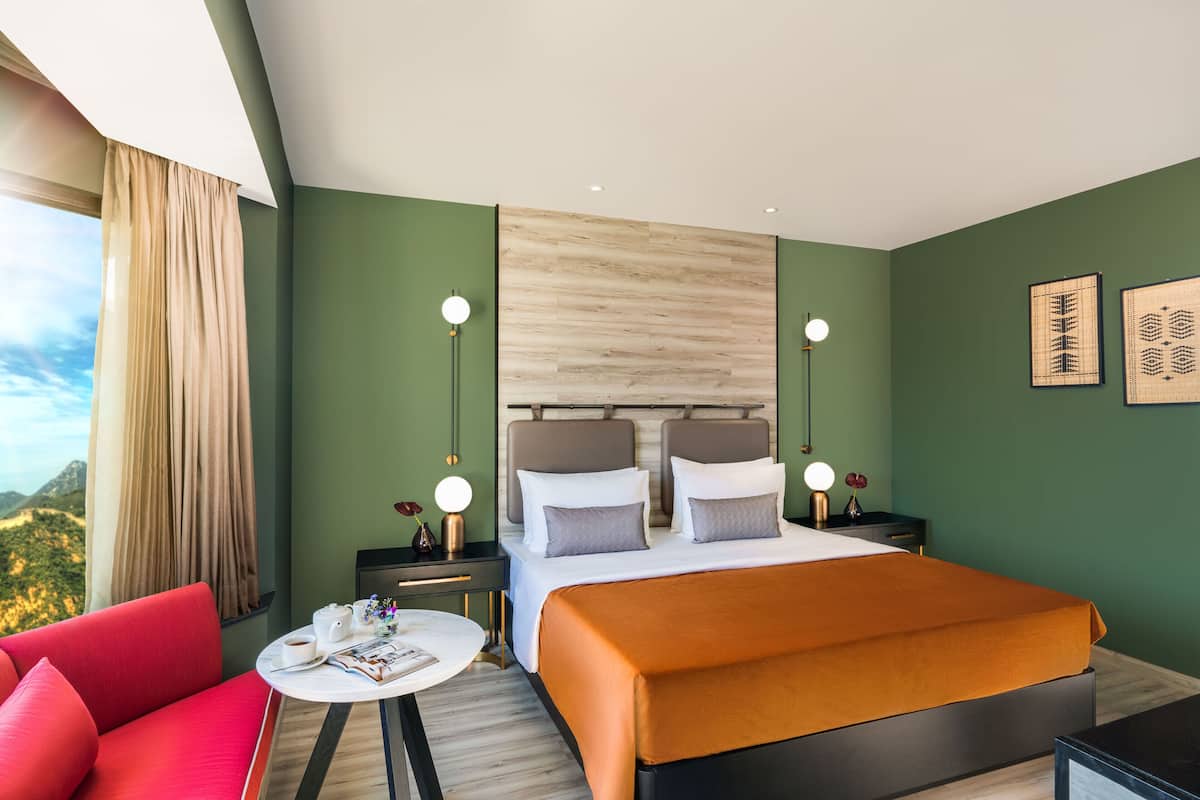 Ein Hotelzimmer mit einem großen Bett, einem roten Sofa, einem kleinen Tisch mit einer Zeitschrift und einem Nachttisch mit einer Lampe.