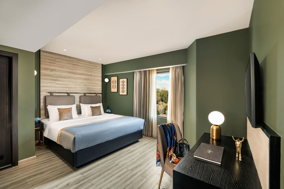 Ein modernes Hotelzimmer mit einem großen Bett, einem Schreibtisch mit Lampe, einem Fernseher und Blick ins Freie.