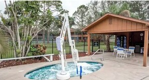 Relax by the pool with a soothing water fountain nearby, surrounded by lush trees and a covered seating area.