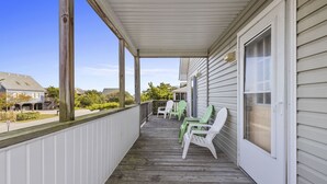 A covered porch with wooden railings, a door, and two green chairs.