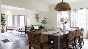 A dining area with a long wooden table, woven chairs, and a hanging light fixture.