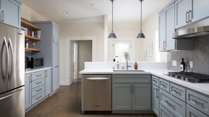 A modern kitchen with grey cabinets, stainless steel appliances, and a herringbone tile backsplash.