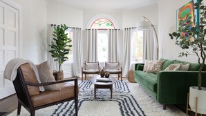A living room with a green sofa, a brown leather chair, a white rug, and a large window with curtains.