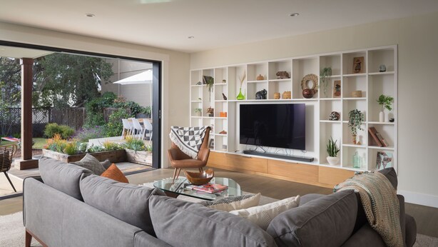 A modern living room with a grey sofa, a glass coffee table, and a TV on a white shelf.