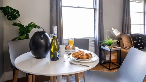 A modern dining area with a round table, a vase, a bottle, and a plate of croissants. - Bateman, modern City centre apartment sleeps 6 (York)