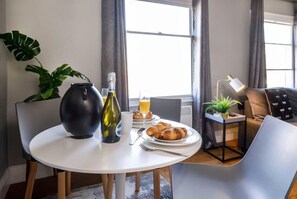 Un comedor moderno con una mesa redonda, un florero, una botella y un plato de croissants.