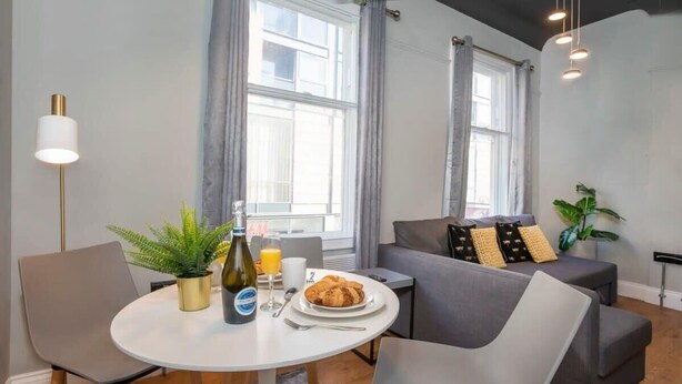 A modern living room with a round dining table, grey sofas, and a potted plant.