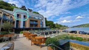 A modern outdoor patio area with wooden furniture, a glass balustrade, and a view of the sea.