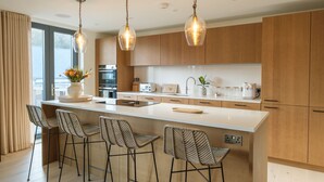 A modern kitchen with a large island, bar stools, wooden cabinets, and pendant lighting.