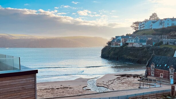 A coastal view with a beach, a building with multiple stories, and a clear sky.