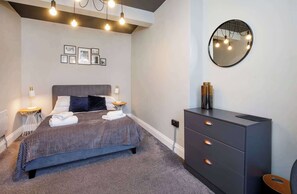 Un dormitorio moderno con cama, lámparas de noche, cómoda, espejo y cuadros en la pared.