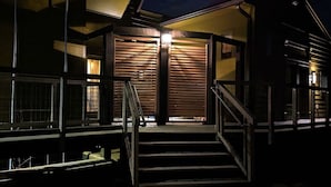 Un bâtiment moderne avec un escalier menant à une porte en bois, des rampes en métal et un intérieur éclairé.