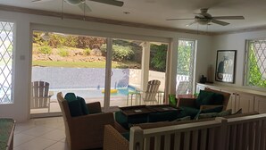 A spacious room with a view of a swimming pool, two ceiling fans, wicker furniture, and a dining table.