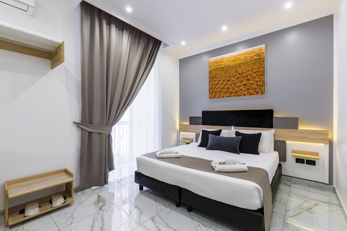 Une chambre d’hôtel moderne dotée d’un grand lit, d’une tête de lit avec éclairage intégré, d’une table de chevet et d’une œuvre d’art accrochée au mur.