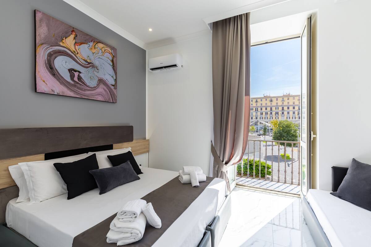 Une chambre d’hôtel moderne, équipée d’un lit, d’un tableau, d’un climatiseur et d’un balcon offrant une vue sur la ville.