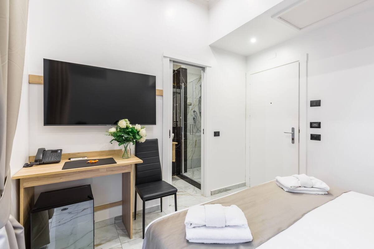 Une chambre d’hôtel comprenant un lit, un bureau avec un téléphone, une chaise, une télévision, une douche et une armoire.