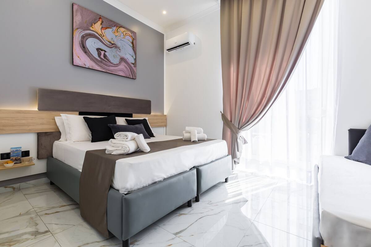 Une chambre d’hôtel moderne avec un grand lit, une tête de lit, une table de chevet et un climatiseur fixé au mur.