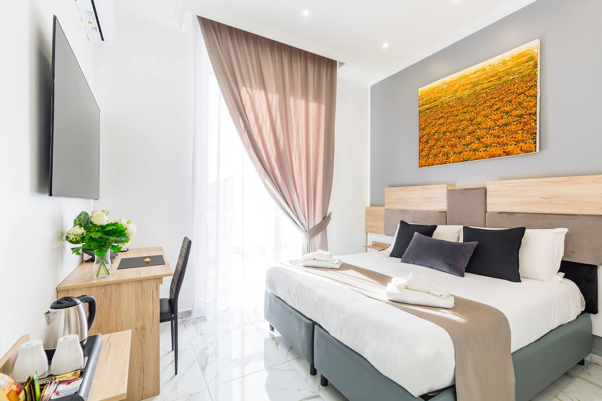 Une chambre d’hôtel moderne, équipée d’un lit, d’une table de chevet et d’une grande fenêtre avec des rideaux.