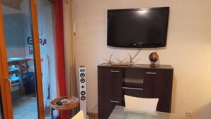 Una habitación con una mesa de vidrio, un mueble de madera oscura con un televisor de pantalla plana montado encima, y una pequeña mesa redonda con un globo terráqueo y decoración de cuernos.