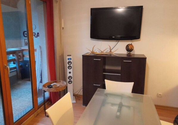 Ein Zimmer mit einem Glastisch, einer dunklen Holzkommode mit einem flachbildfernseher darüber und einem kleinen runden Tisch mit Globus und Geweihdeko.