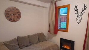 Una habitación acogedora con sofá, un reloj de pared de madera, chimenea y decoración de cabeza de ciervo.